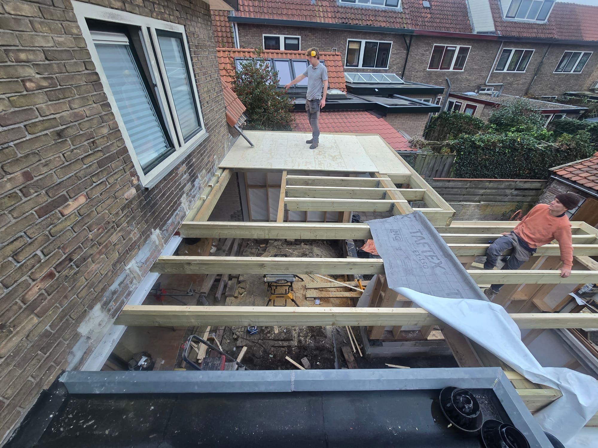 Twee dakdekkers werken aan een nieuwe houten dakconstructie van een aanbouw