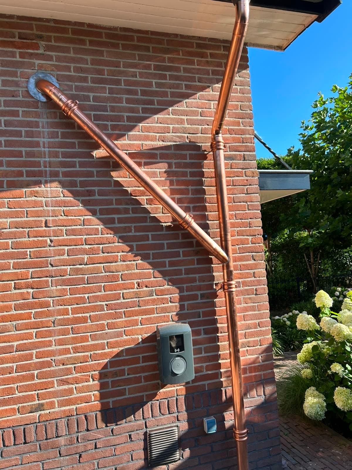 Koperen hemelwaterafvoer met gesoldeerde verbindingen en koperen beugels tegen een bakstenen muur