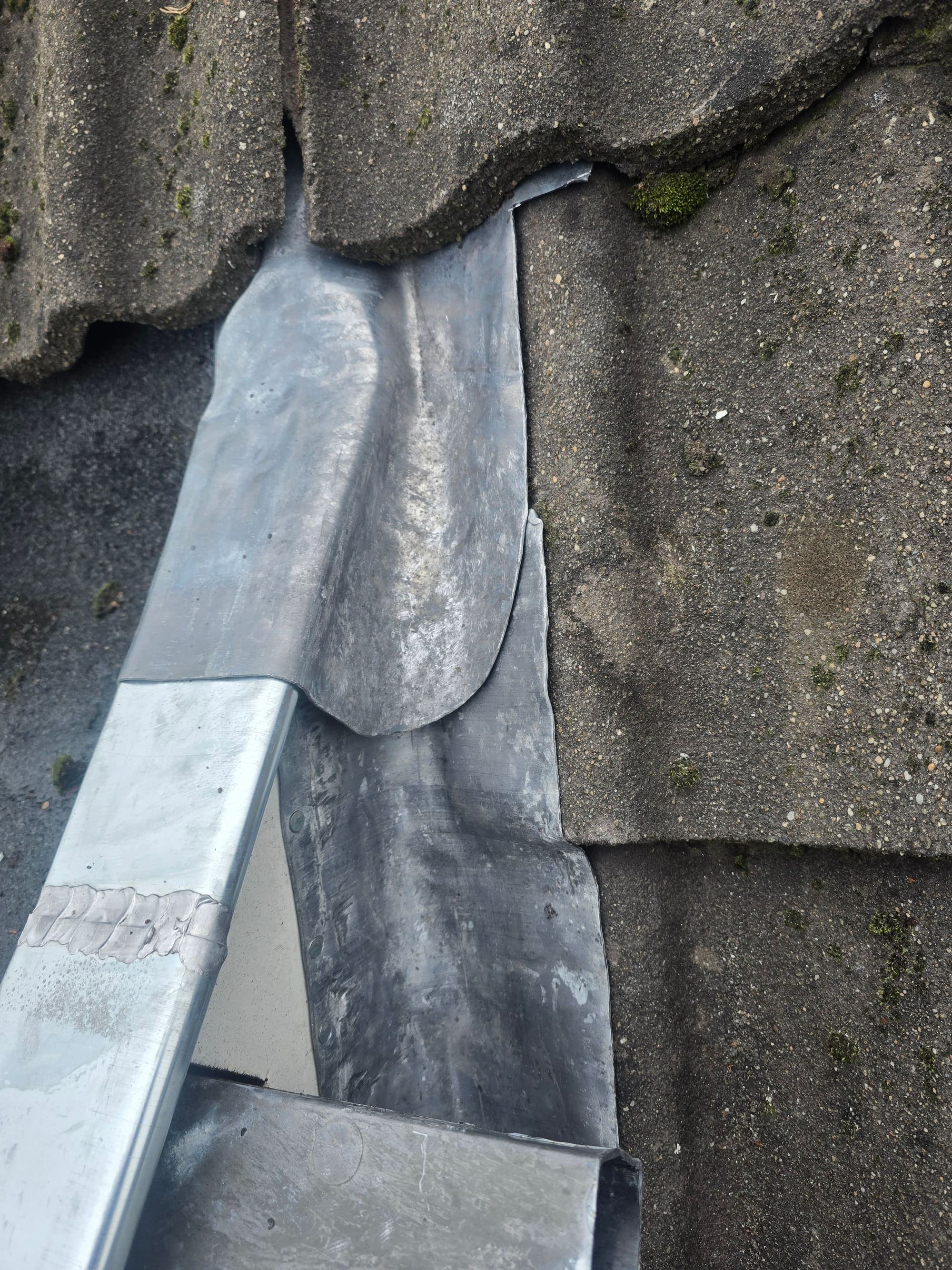Met de hand gezet loodwerk tussen betonnen dakpannen en een zinken goot